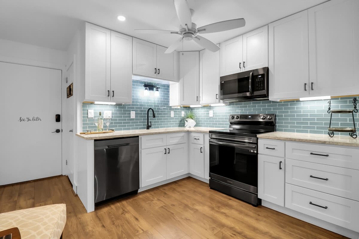 Renovated kitchen with sea-glass tile backsplash, quartz counters, and stainless appliances